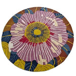 A vibrant, hand-tufted round area rug featuring a striking floral design with a large central bloom in pink, accented by yellow, blue, and brown petals. This wool rug is perfect for adding a splash of color and style to your dining room or office space.