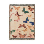 Woven throw blanket scattered with multicolored butterflies in pink, teal, blue, gold, and brown on cream linen-textured ground with fringed edges — Vibrant Butterfly Woven Blanket