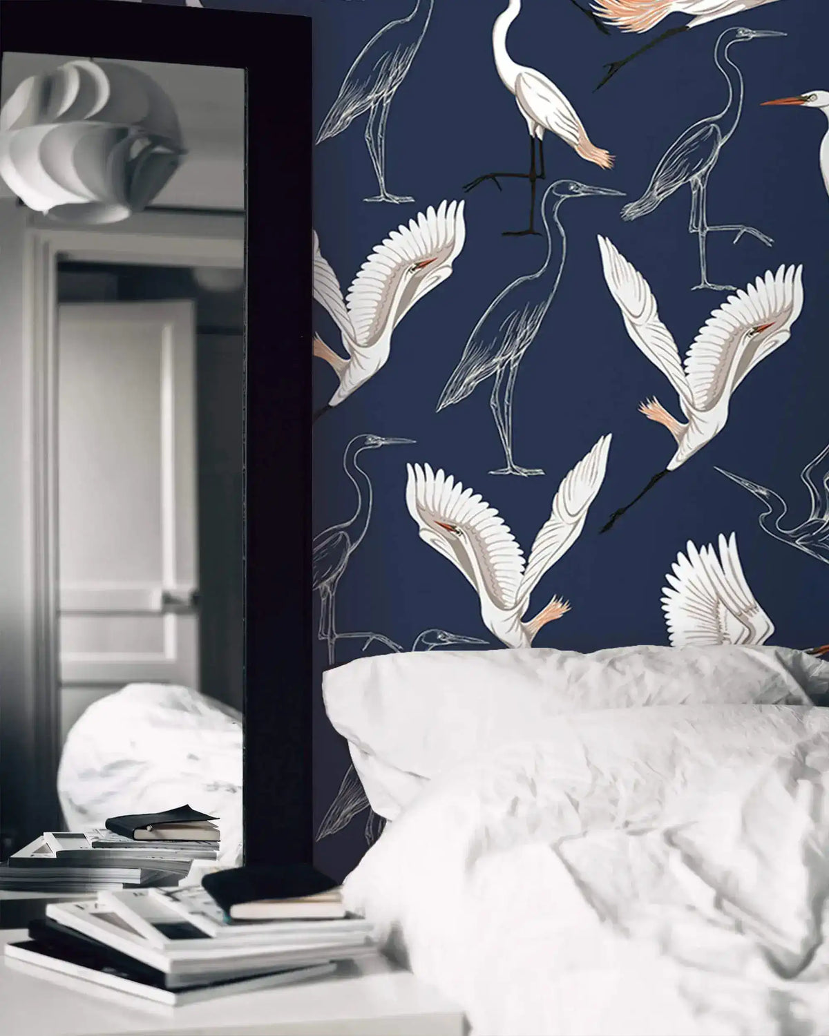 Navy wallpaper with white cranes behind white bedding with tall floor mirror and books