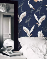 Navy wallpaper with white cranes behind white bedding with tall floor mirror and books
