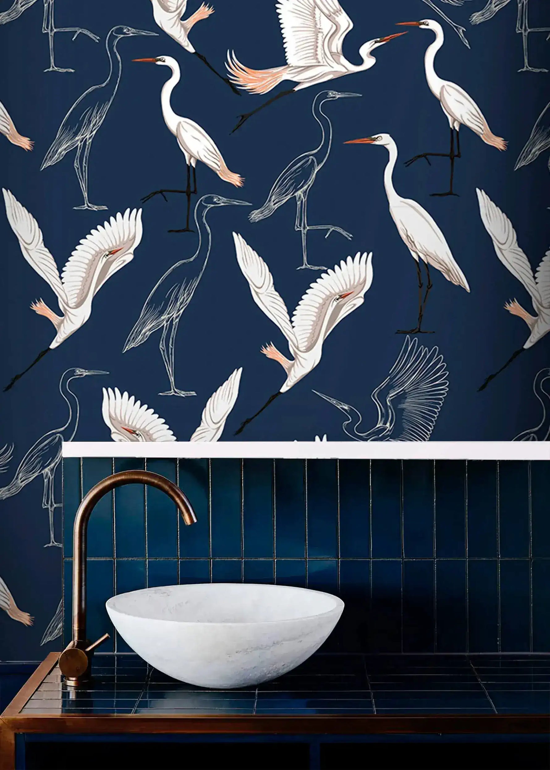 Navy wallpaper with white cranes above blue tiled bathroom vanity with marble basin and brass tap