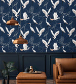 Navy wallpaper with white flying cranes above panelling with copper pendant lamps and tan leather seat