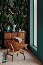 Vibrant fern canopy wallpaper accent wall with carved cabinet, wood chairs and teal vases by window