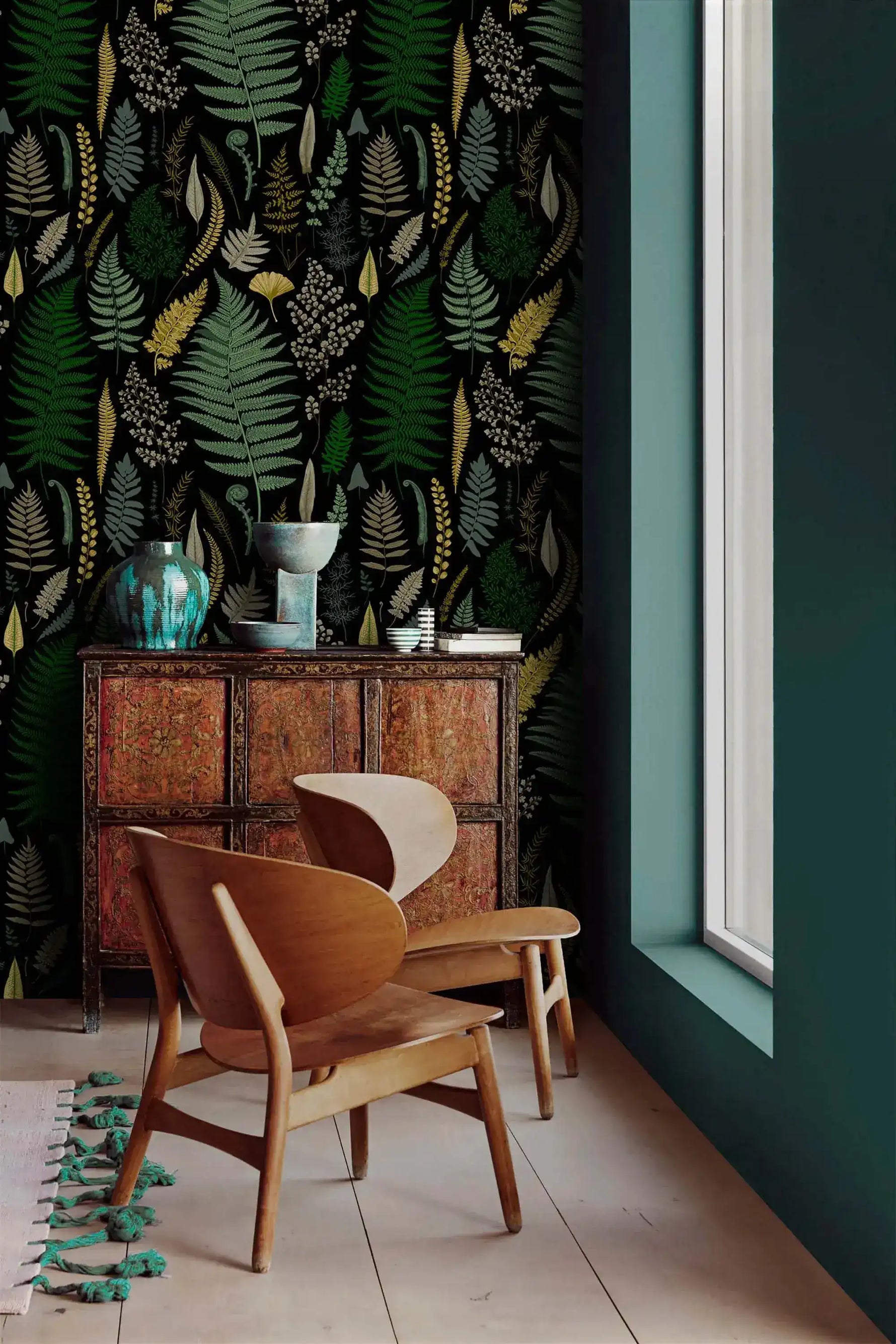 Vibrant fern canopy wallpaper accent wall with carved cabinet, wood chairs and teal vases by window