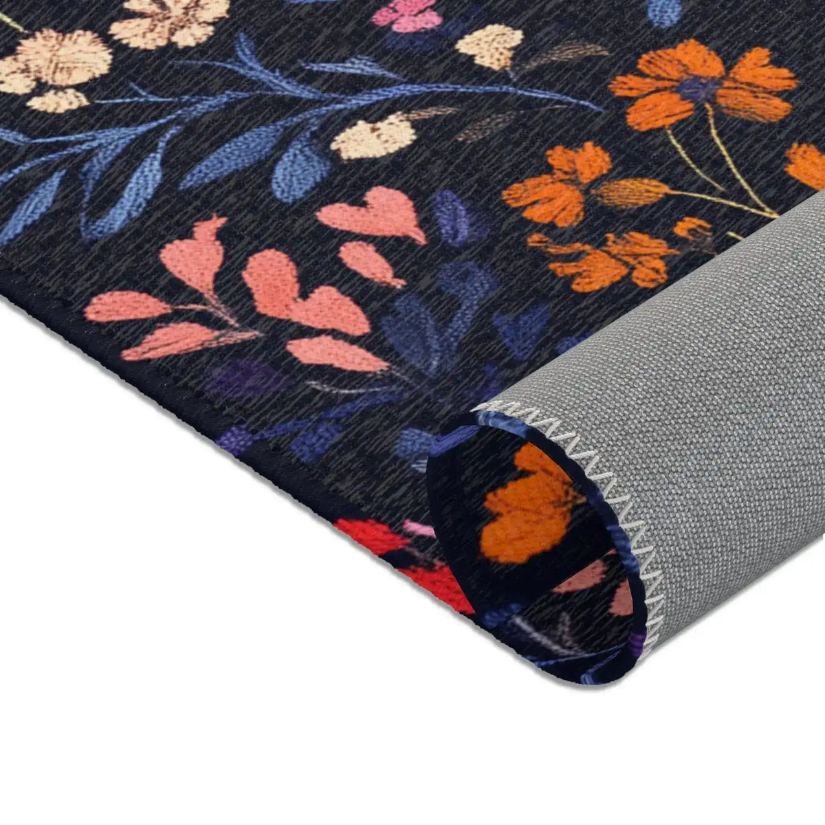 Folded corner of Vibrant Floral Embroidered Accent Rug showing orange and pink wildflowers on dark navy, grey non-slip backing at rolled edge