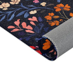 Folded corner of Vibrant Floral Embroidered Accent Rug showing orange and pink wildflowers on dark navy, grey non-slip backing at rolled edge