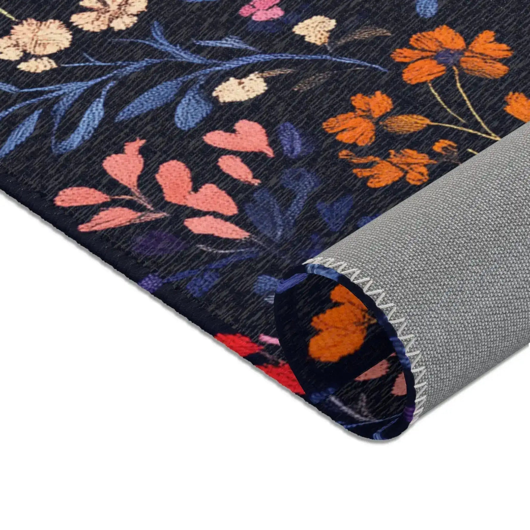Folded corner of Vibrant Floral Embroidered Accent Rug showing orange and pink wildflowers on dark navy, grey non-slip backing at rolled edge