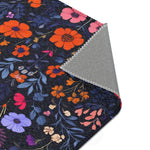 Corner of Vibrant Floral Embroidered Accent Rug with orange and purple wildflowers on dark navy, rolled corner reveals grey non-slip backing