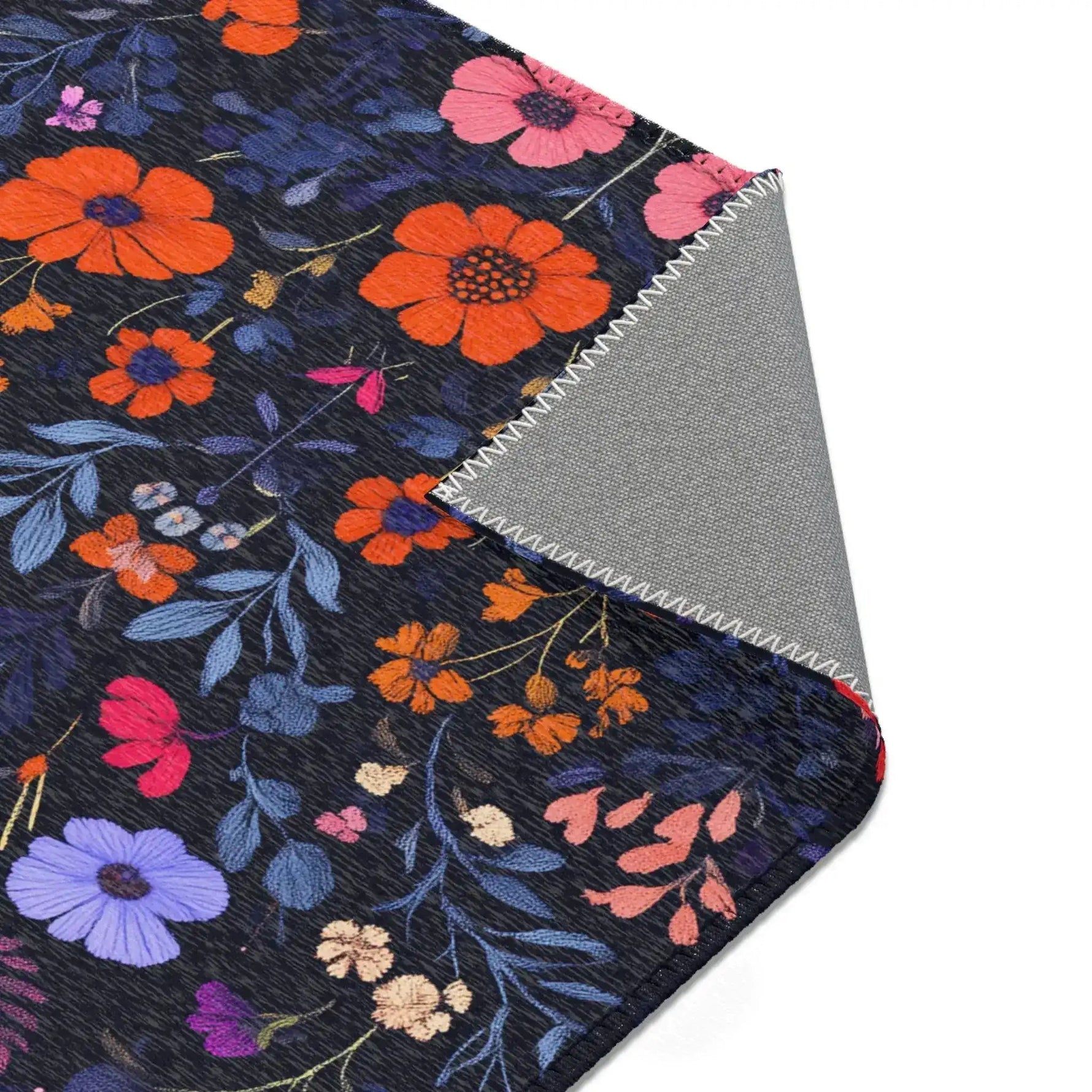 Corner of Vibrant Floral Embroidered Accent Rug with orange and purple wildflowers on dark navy, rolled corner reveals grey non-slip backing