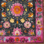 A vibrant floral tapestry area rug featuring a hand-knotted wool design. This large living room rug showcases a rich array of pink, orange, and yellow flowers on a dark background, framed by a bold pink border. Perfect for adding a touch of Persian elegance to any living room, especially in an 8x10 space. This vintage-style wool rug is ideal for those seeking large area rugs with a floral motif.
