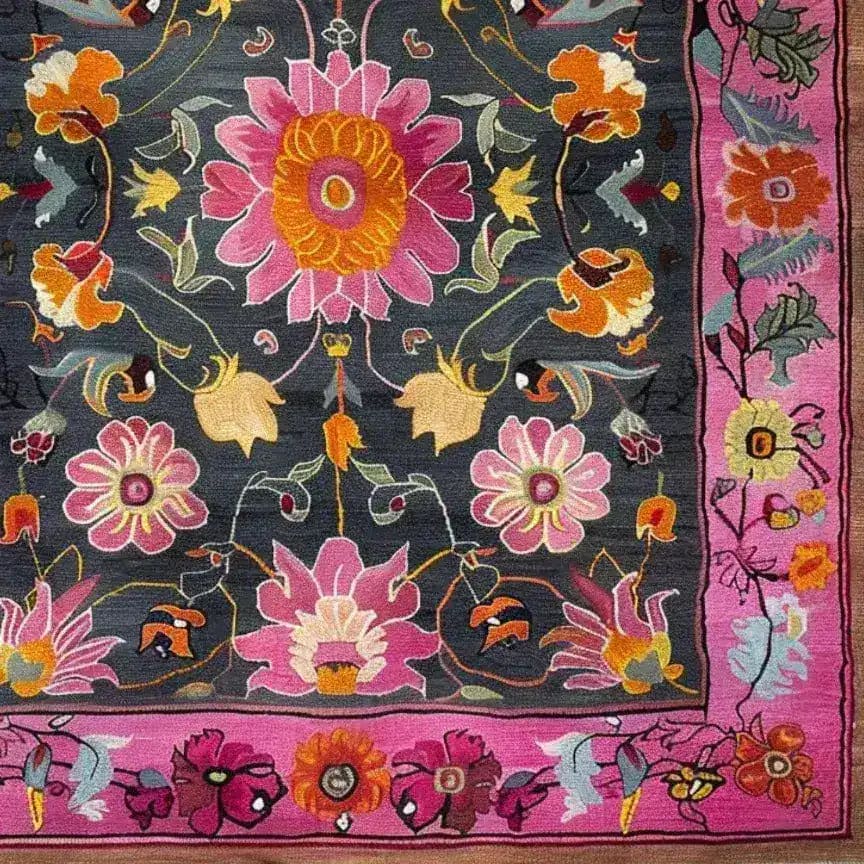 A vibrant floral tapestry area rug featuring a hand-knotted wool design. This large living room rug showcases a rich array of pink, orange, and yellow flowers on a dark background, framed by a bold pink border. Perfect for adding a touch of Persian elegance to any living room, especially in an 8x10 space. This vintage-style wool rug is ideal for those seeking large area rugs with a floral motif.