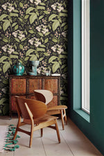 Dark floral wallpaper with white blooms in corner with carved wood cabinet, teal vases and wood chair