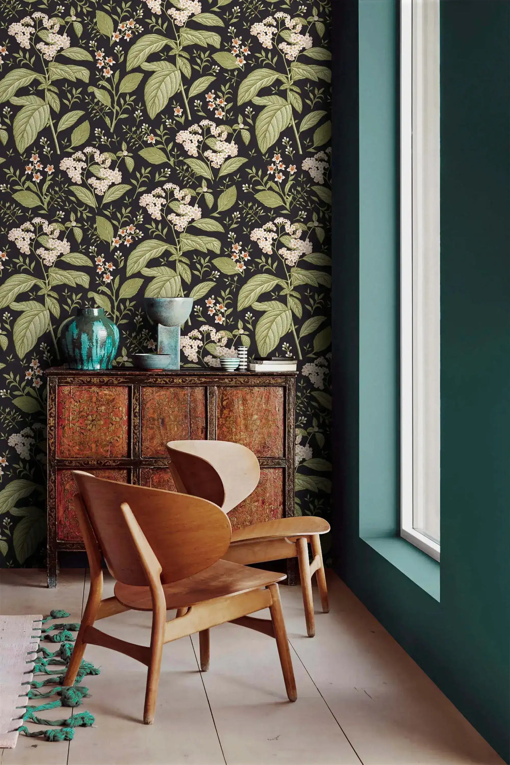 Dark floral wallpaper with white blooms in corner with carved wood cabinet, teal vases and wood chair