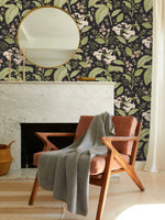 Dark floral wallpaper with white blooms above marble fireplace with round mirror and rust velvet chair