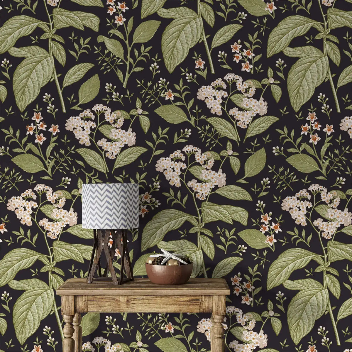 Close-up dark floral wallpaper with white blooms and green leaves behind rustic table with chevron lamp