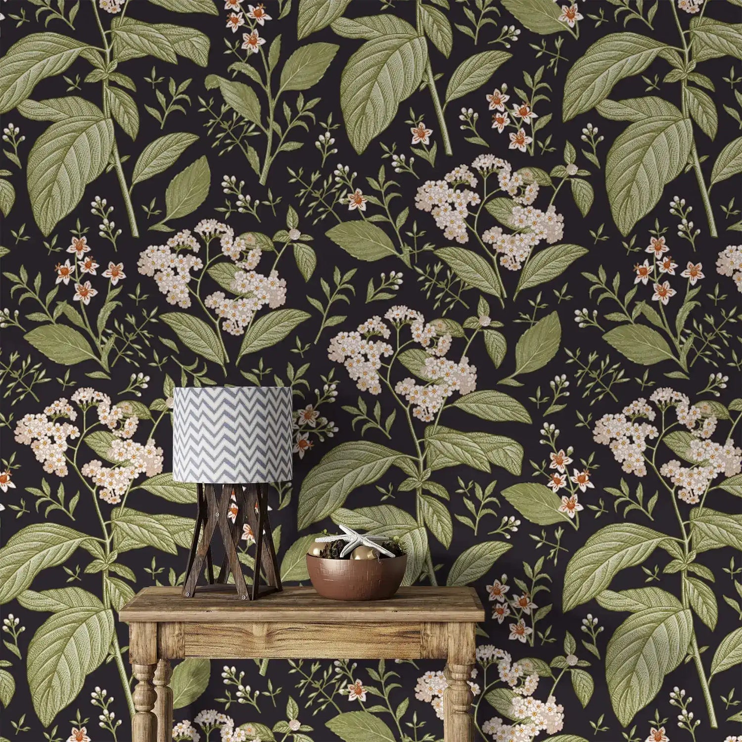 Close-up dark floral wallpaper with white blooms and green leaves behind rustic table with chevron lamp