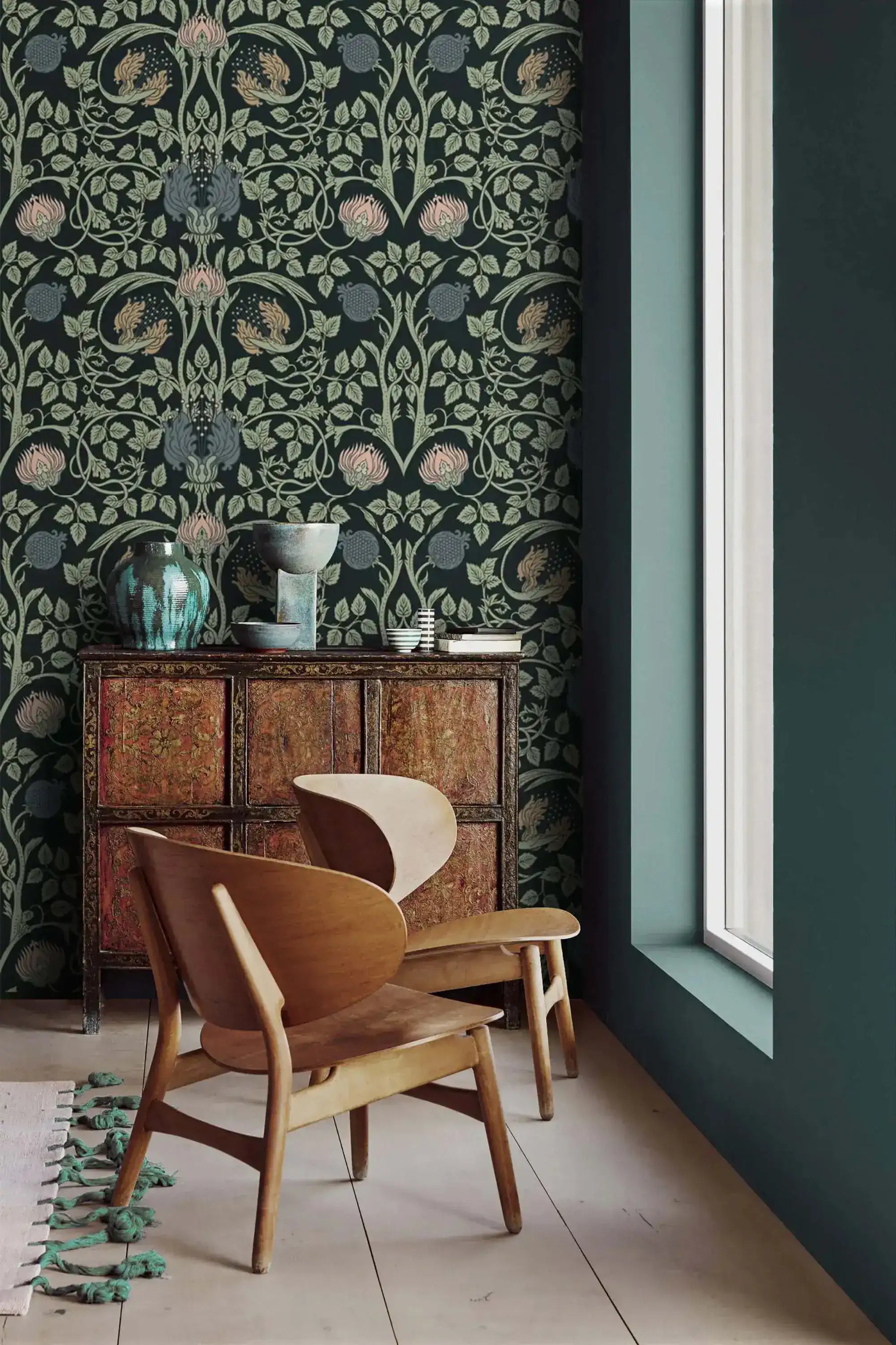Vine and flower wallpaper corner with wooden lounge chair, antique cabinet topped with teal glazed vase, and teal wall