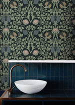 Vine and flower wallpaper in bathroom above dark blue vertical tiles with white marble basin and bronze gooseneck faucet
