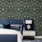 Vine and flower wallpaper behind navy upholstered bed with silver nightstand, agate table lamp, and reading sconce