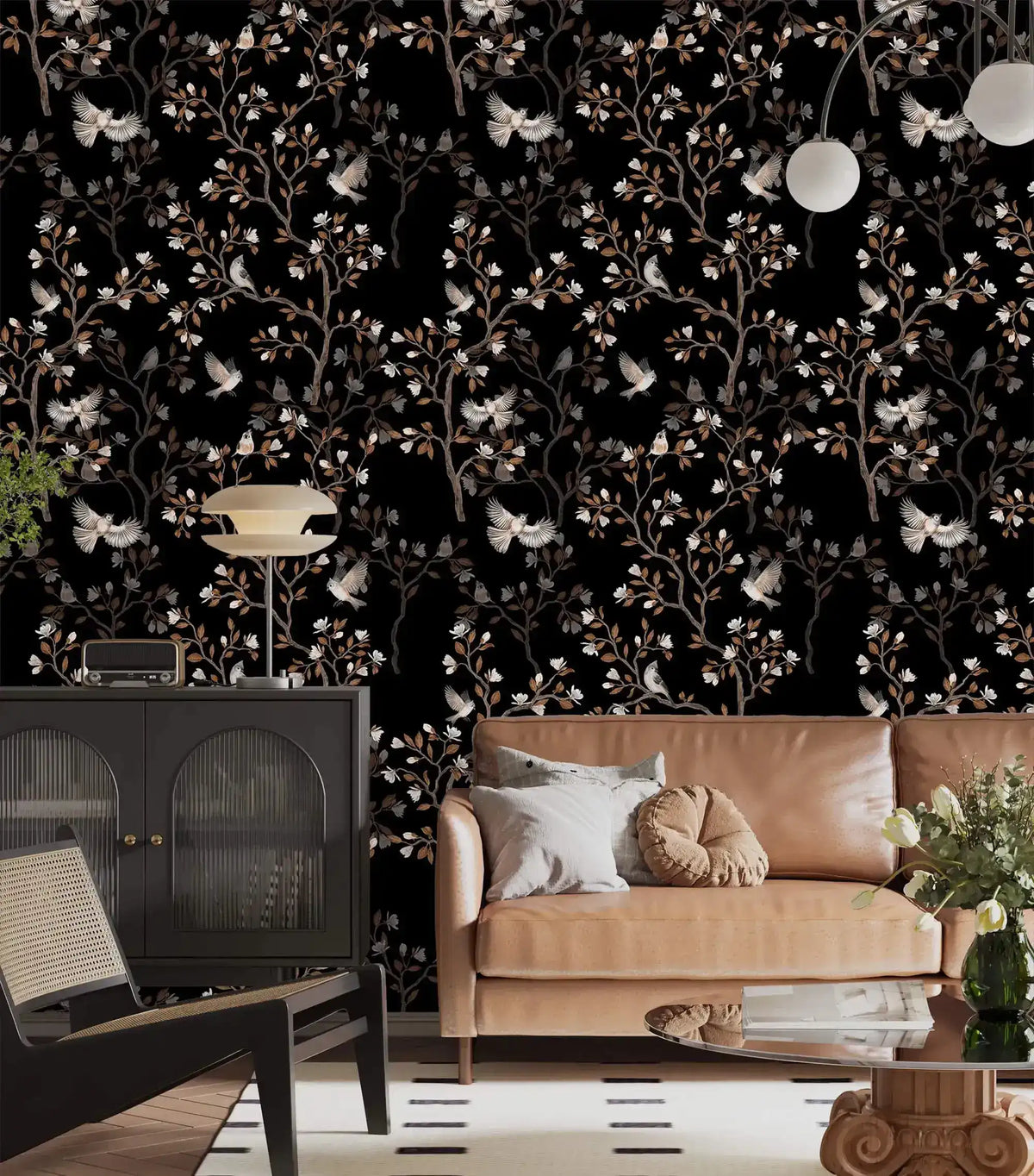 Vintage bird haven wallpaper with birds and blossoms on black behind a tan leather sofa and black cabinet