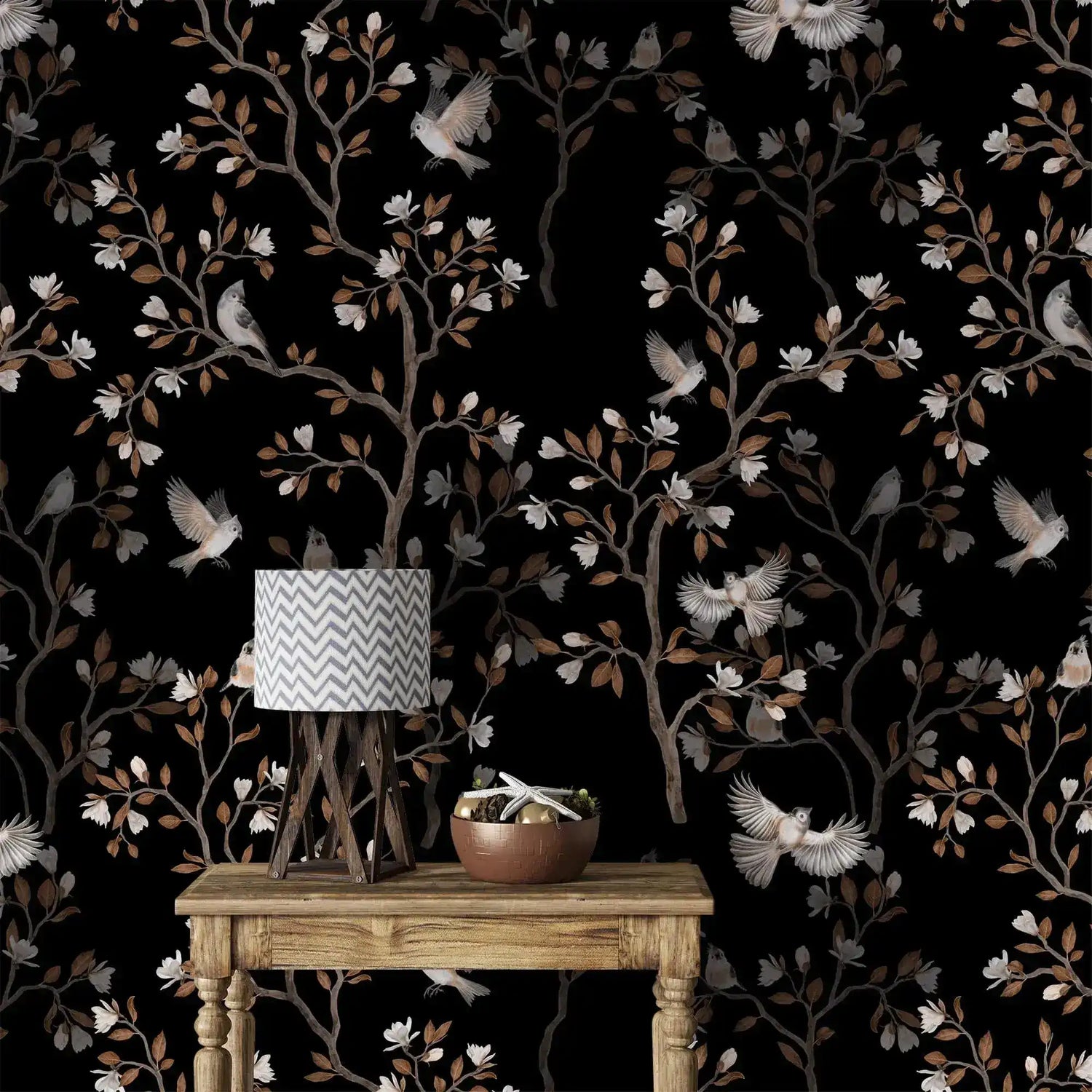 Vintage bird haven wallpaper with birds, blossoms and branches on black behind a rustic wood table and lamp