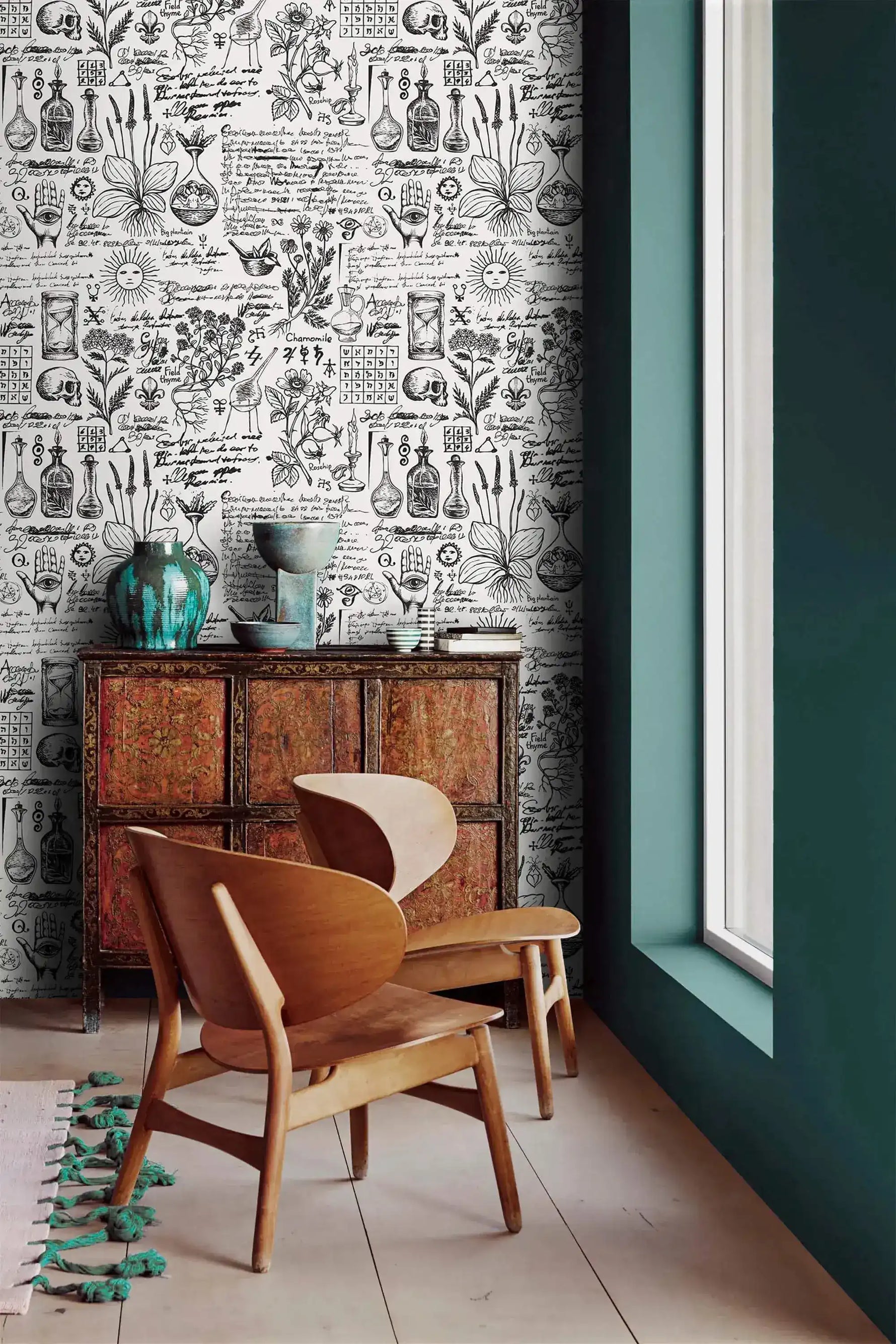 Vintage herbal alchemy wallpaper next to a teal wall with antique cabinet and curved wood chairs