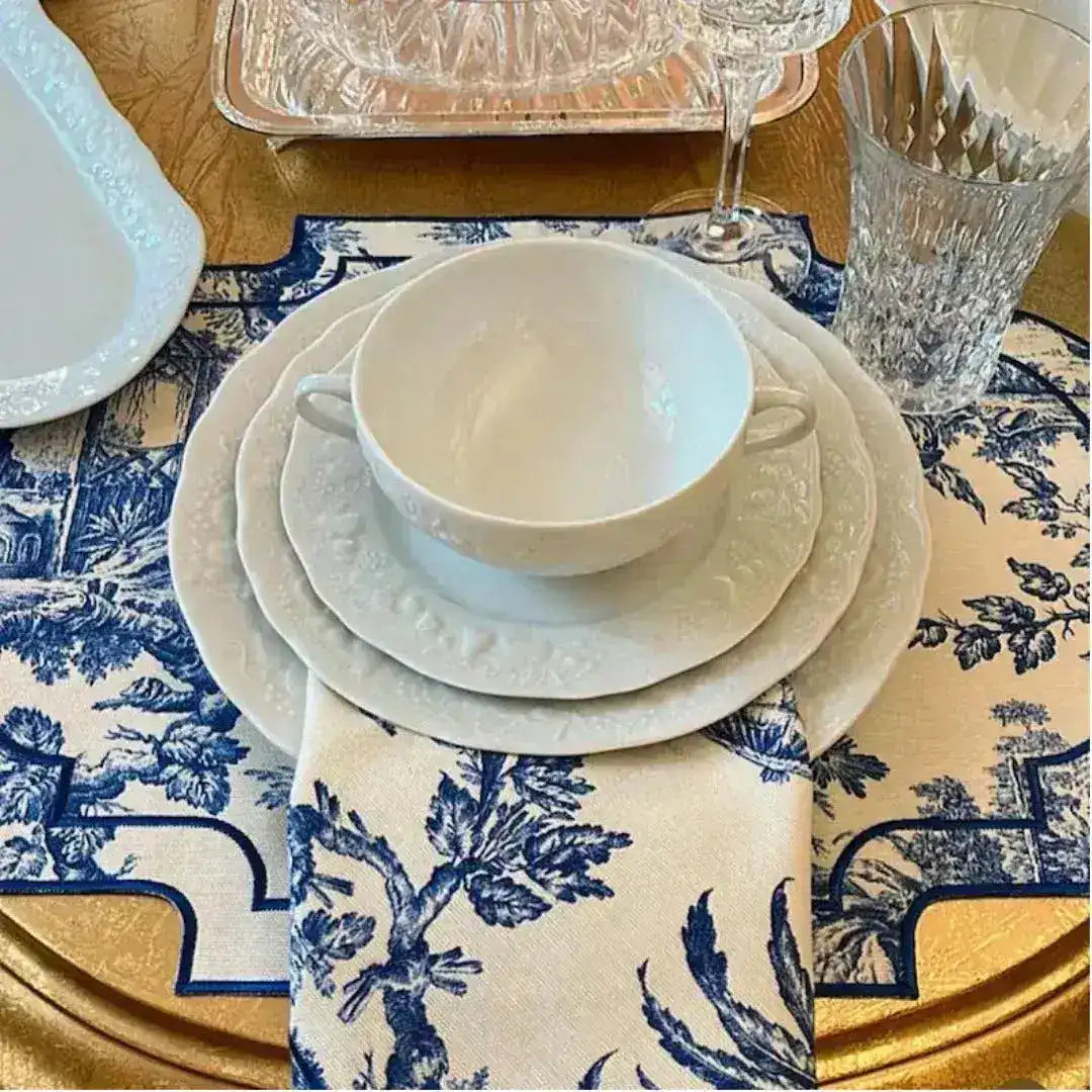 Vintage-Inspired Placemats in blue-white toile pattern with navy border, styled with white dinnerware on gold table