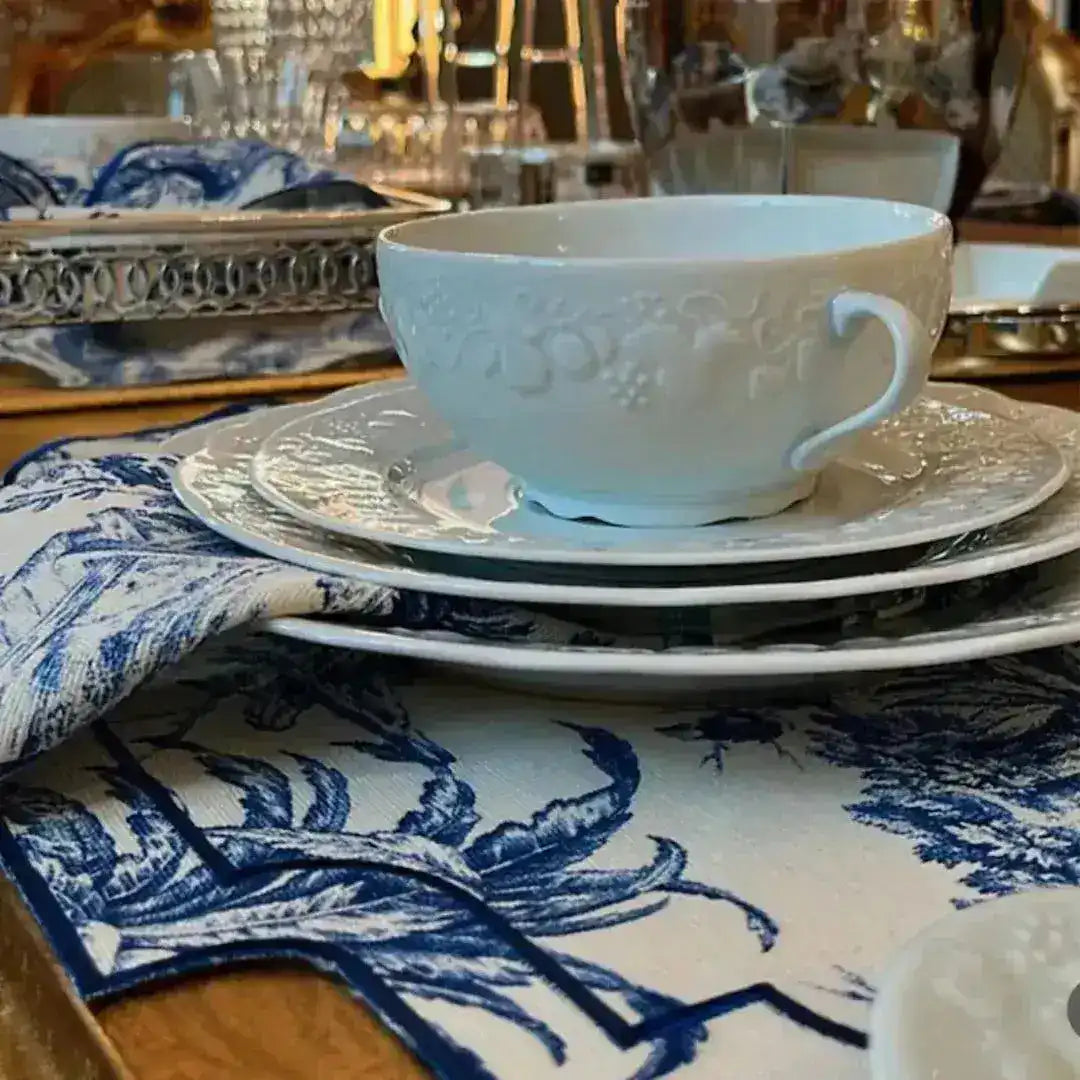 Vintage-Inspired Placemats close-up — blue-white toile scenic print with navy border, white embossed cup stacked on plates