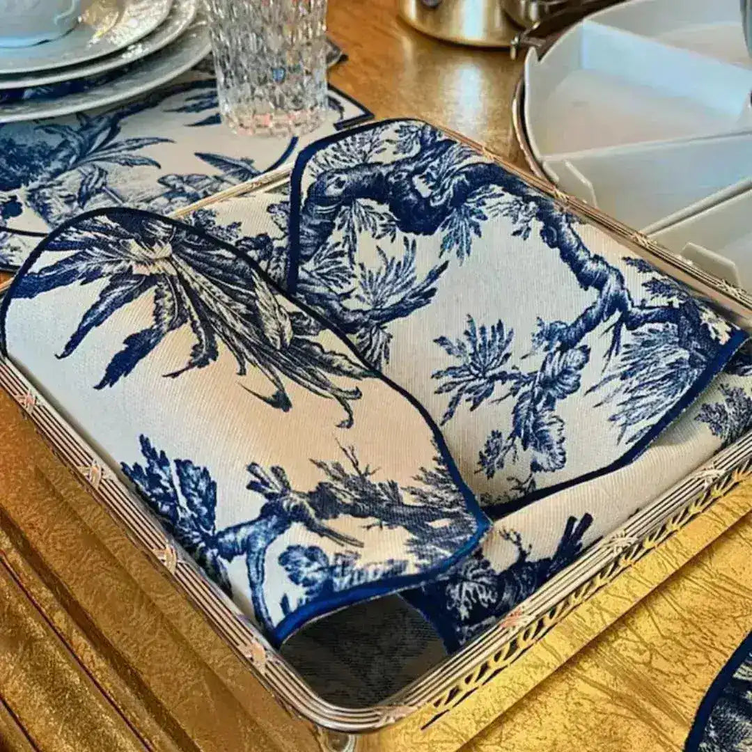 Vintage-Inspired Placemats stacked and folded on silver tray — blue-white toile scenic fabric with navy piped edges