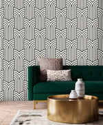 Vintage ornate outline wallpaper, black art deco arches on cream behind an emerald velvet sofa