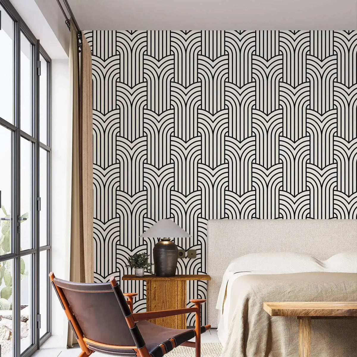 Vintage ornate outline wallpaper in a bedroom, black art deco arches on cream behind an upholstered bed
