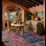 A beautifully styled living room features a Vintage Radiance Hand Knotted Area Rug, perfect for adding a touch of elegance to any space. This Persian rug, sized 8x10, showcases intricate designs in vibrant colors, making it ideal for living rooms. The cozy setting includes a wooden table, chairs, and plush sofa, complementing the rug's vintage charm.