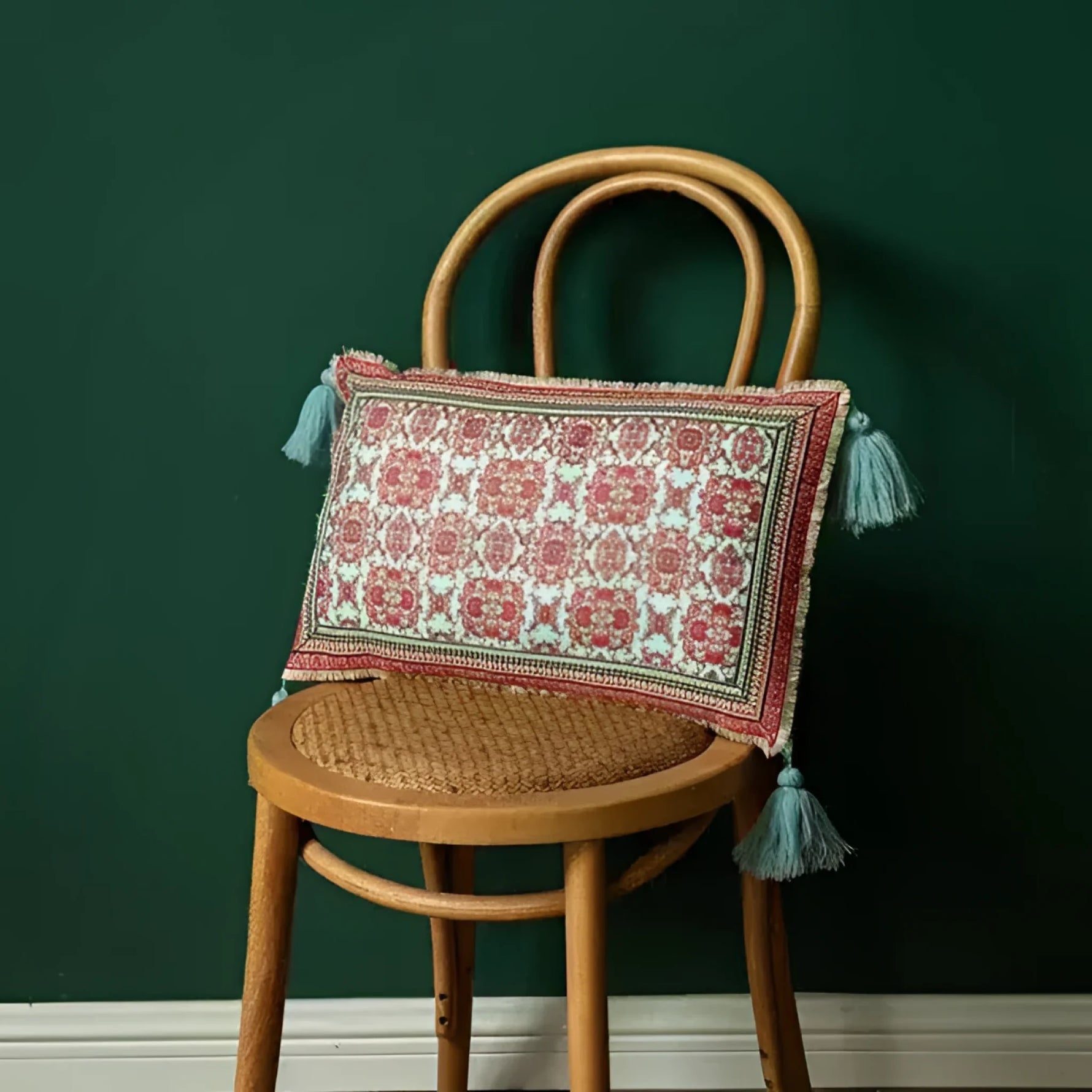 Vintage velvet floral throw pillow with tassels on a wooden chair against a green wall.