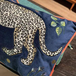 Decorative throw pillow featuring a walking leopard design on a blue background with green leaves and floral accents.