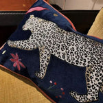 Decorative throw pillow featuring a walking leopard design against a blue jungle background, accented with colorful floral elements.