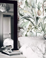 Watercolor tropical jungle wallpaper behind white bedding with tall floor mirror and books