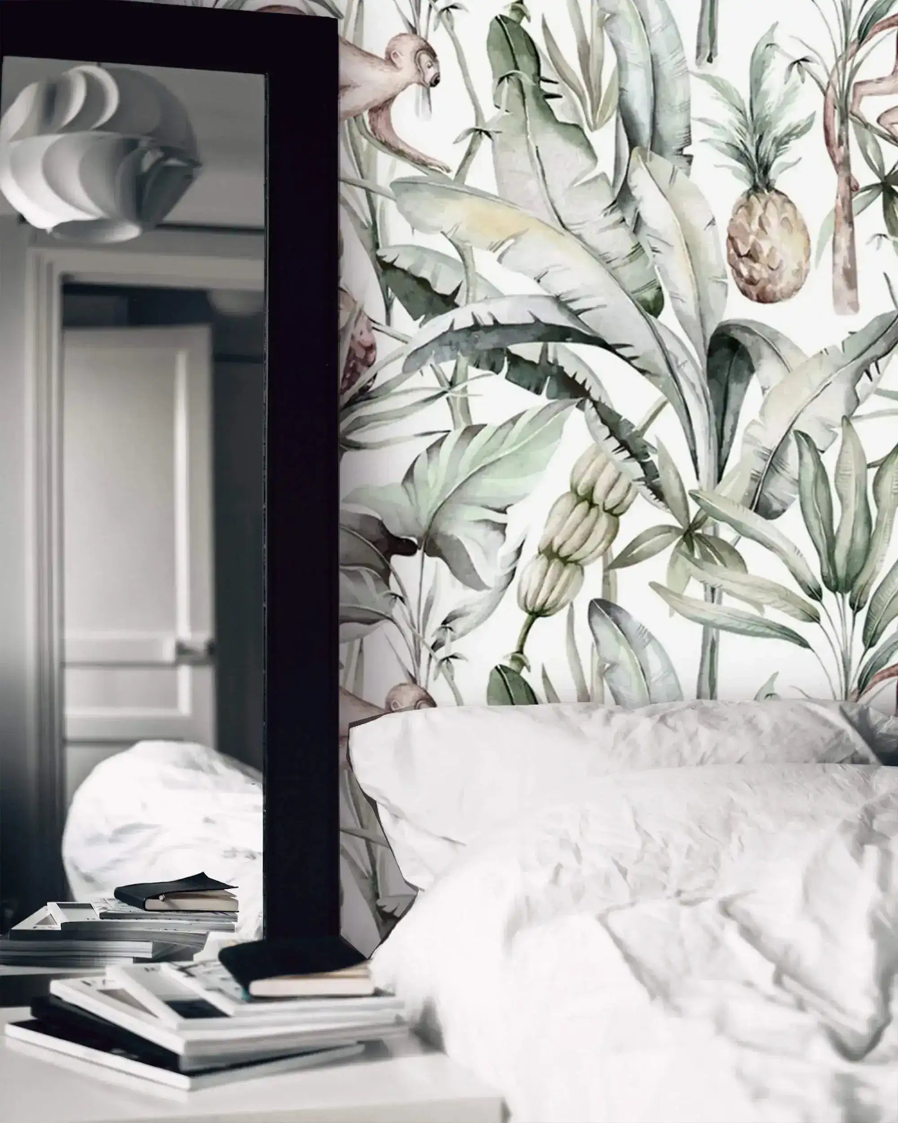 Watercolor tropical jungle wallpaper behind white bedding with tall floor mirror and books