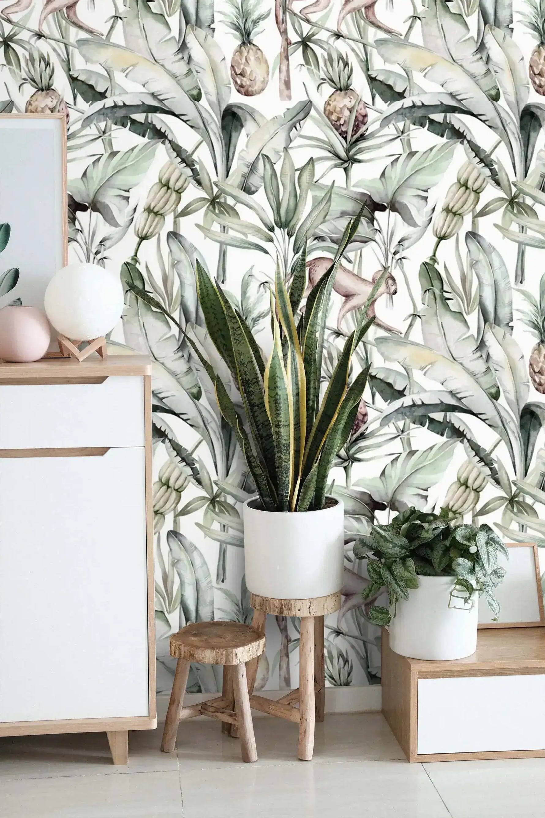 Watercolor tropical jungle wallpaper behind white sideboard with snake plant and wood stool