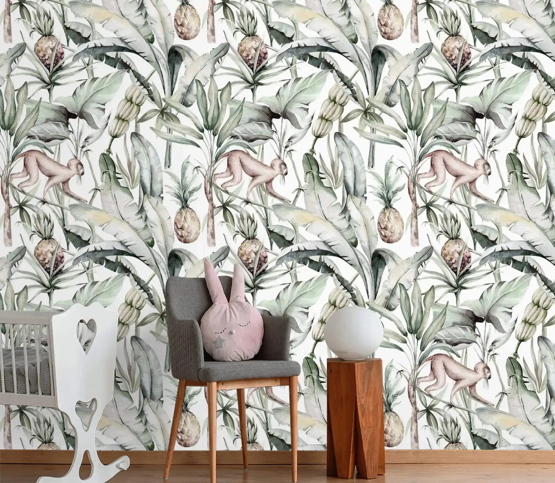 Watercolor tropical jungle wallpaper with monkeys and pineapples in nursery with grey chair and crib