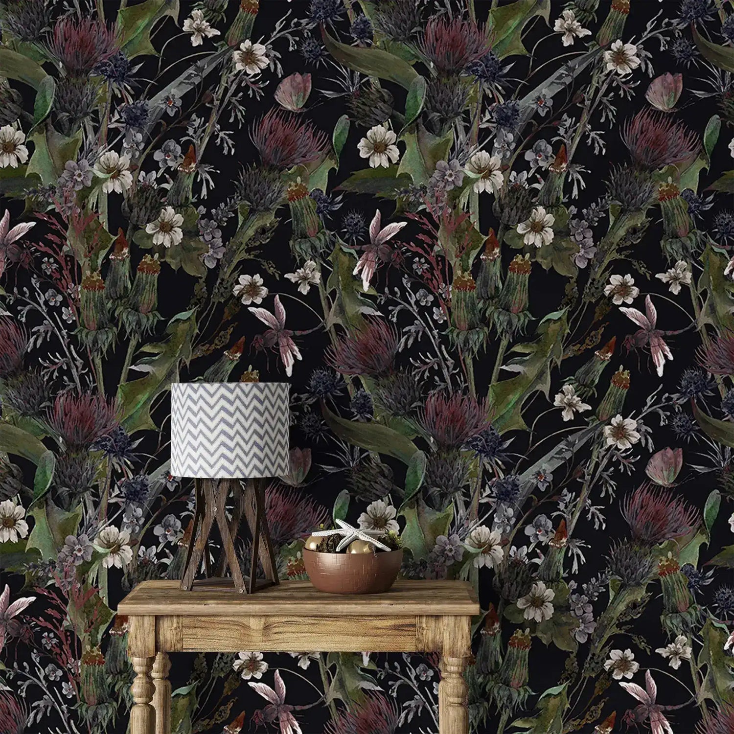 Whimsical vintage garden wallpaper with daisies, thistles and foliage on black behind a rustic wood table and lamp