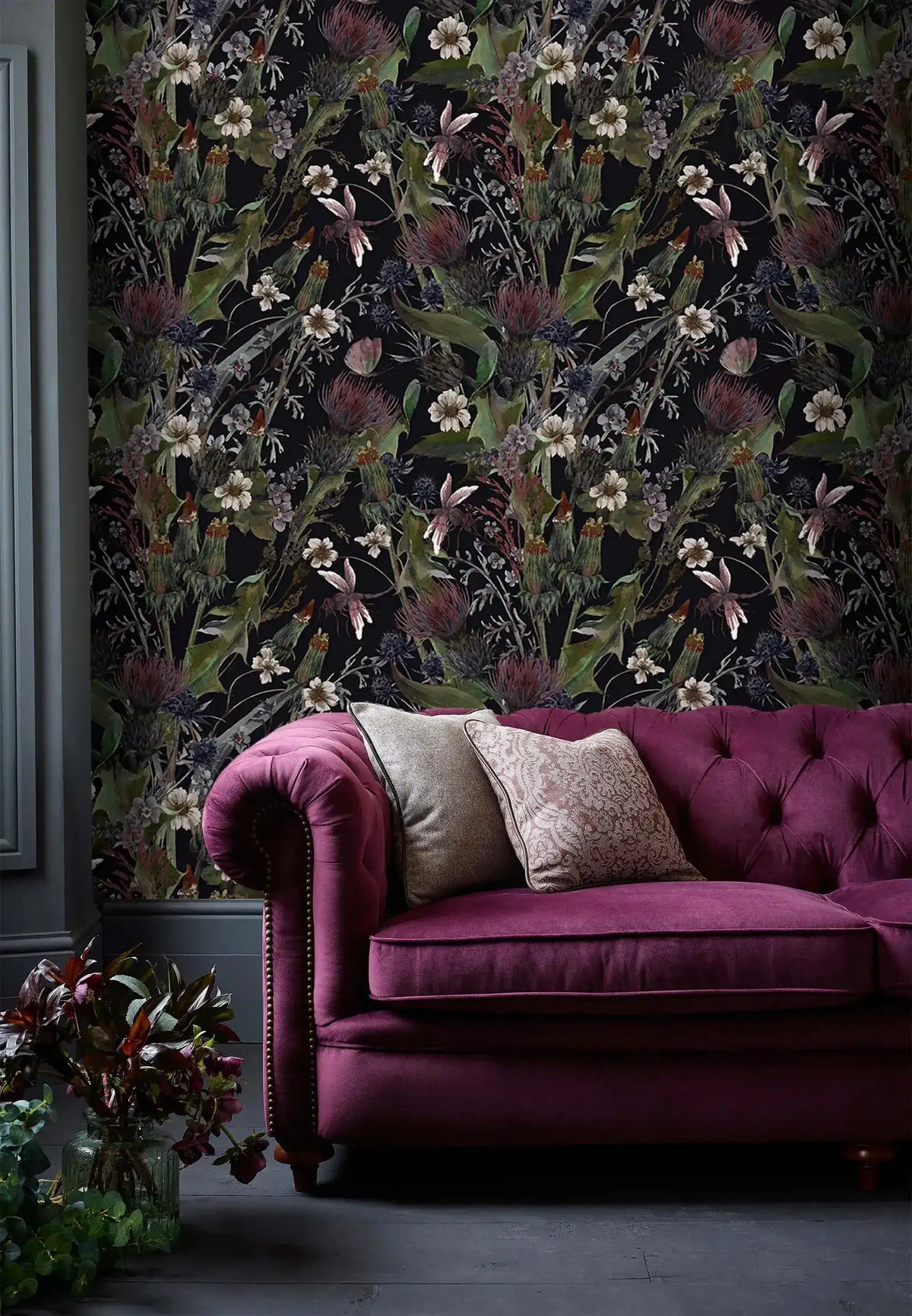 Whimsical vintage garden wallpaper with dark florals on black behind a berry velvet tufted Chesterfield sofa