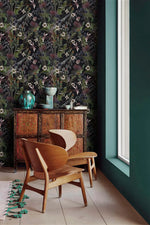 Whimsical vintage garden wallpaper with dark florals on black beside a teal wall and carved wood cabinet