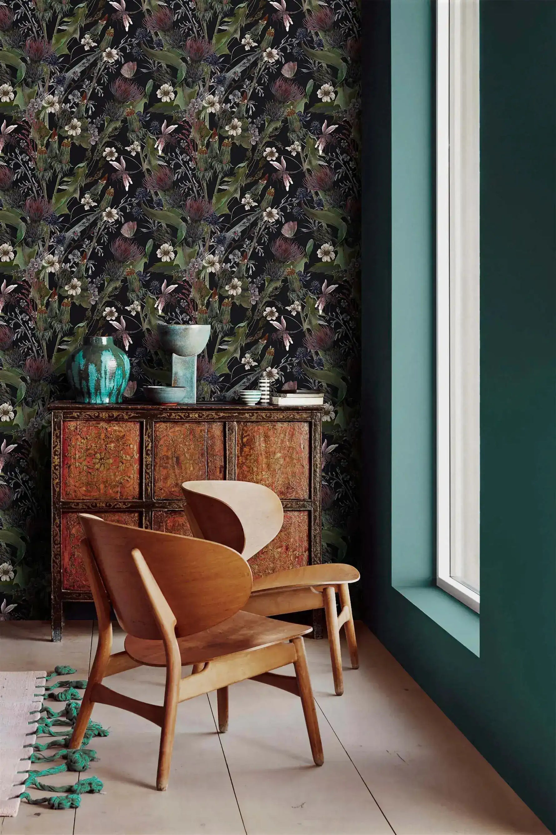Whimsical vintage garden wallpaper with dark florals on black beside a teal wall and carved wood cabinet