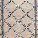 Close-up of the Whispering Vines Hand Knotted Rug, showcasing its intricate wool design with blue and black vine patterns on a cream background. Perfect as an area rug, this vintage-inspired piece is ideal for adding elegance to living room spaces.