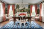 Dining room with a round wooden table, blue cotton rug, chairs, and a large mural on the wall.