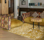 This elegant area rug, titled 'White Bloom Elegant Hand Tufted Viscose Rug - Golden', graces a stylish living room setting. Its intricate patterns and golden hues provide a vintage charm, making it an ideal choice for large living room rugs. Perfect for adding warmth and sophistication, this wool rug complements the vibrant cushions and natural wood accents, creating a cozy and inviting space.