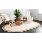 A cozy living room featuring a white oval jute area rug on dark wooden flooring, accompanied by two stylish wooden chairs and a woven basket, creating an inviting space ideal for relaxation.