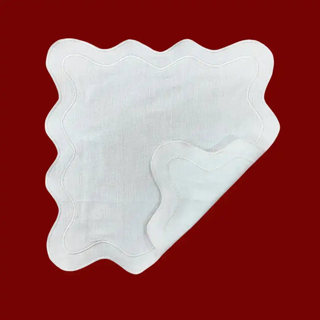 Single white scallop linen square placemat with corner folded to show texture, wavy stitched edge on red background