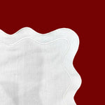 Close-up corner detail of white scallop linen placemat showing wavy border and natural linen weave texture on red