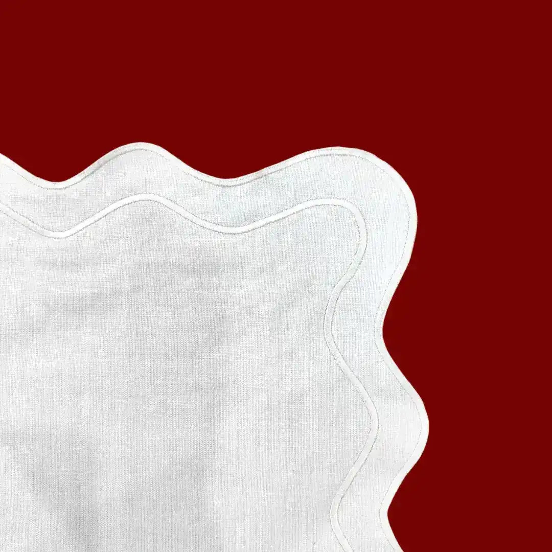 Close-up corner detail of white scallop linen placemat showing wavy border and natural linen weave texture on red